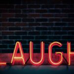Bright neon sign displaying 'LAUGH' against a dark brick wall, creating a vibrant mood.